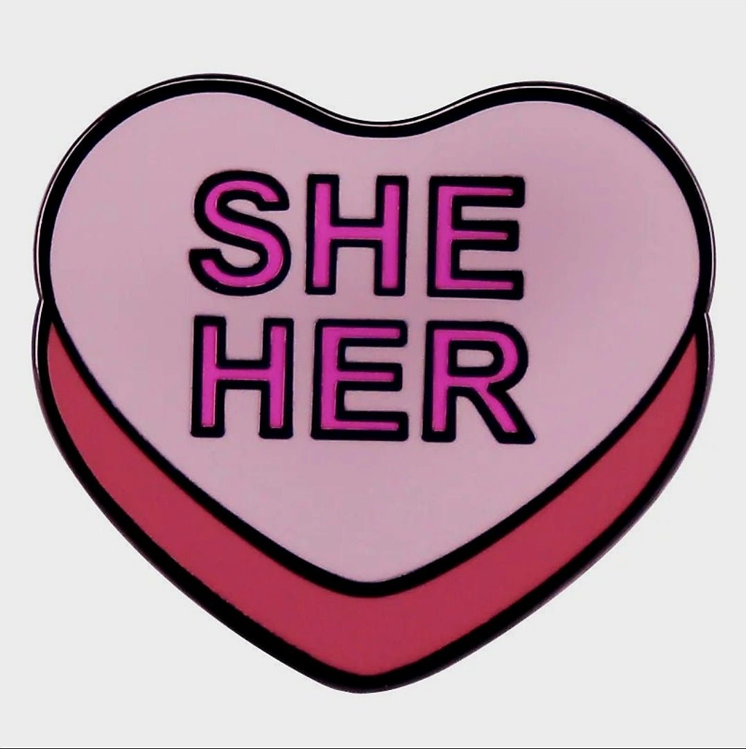 Show your pride in style with the Kiss Me Later She/Her Pronoun Pin—a pink heart-shaped enamel pin with bold SHE HER lettering, a light pink background, and a darker pink border.