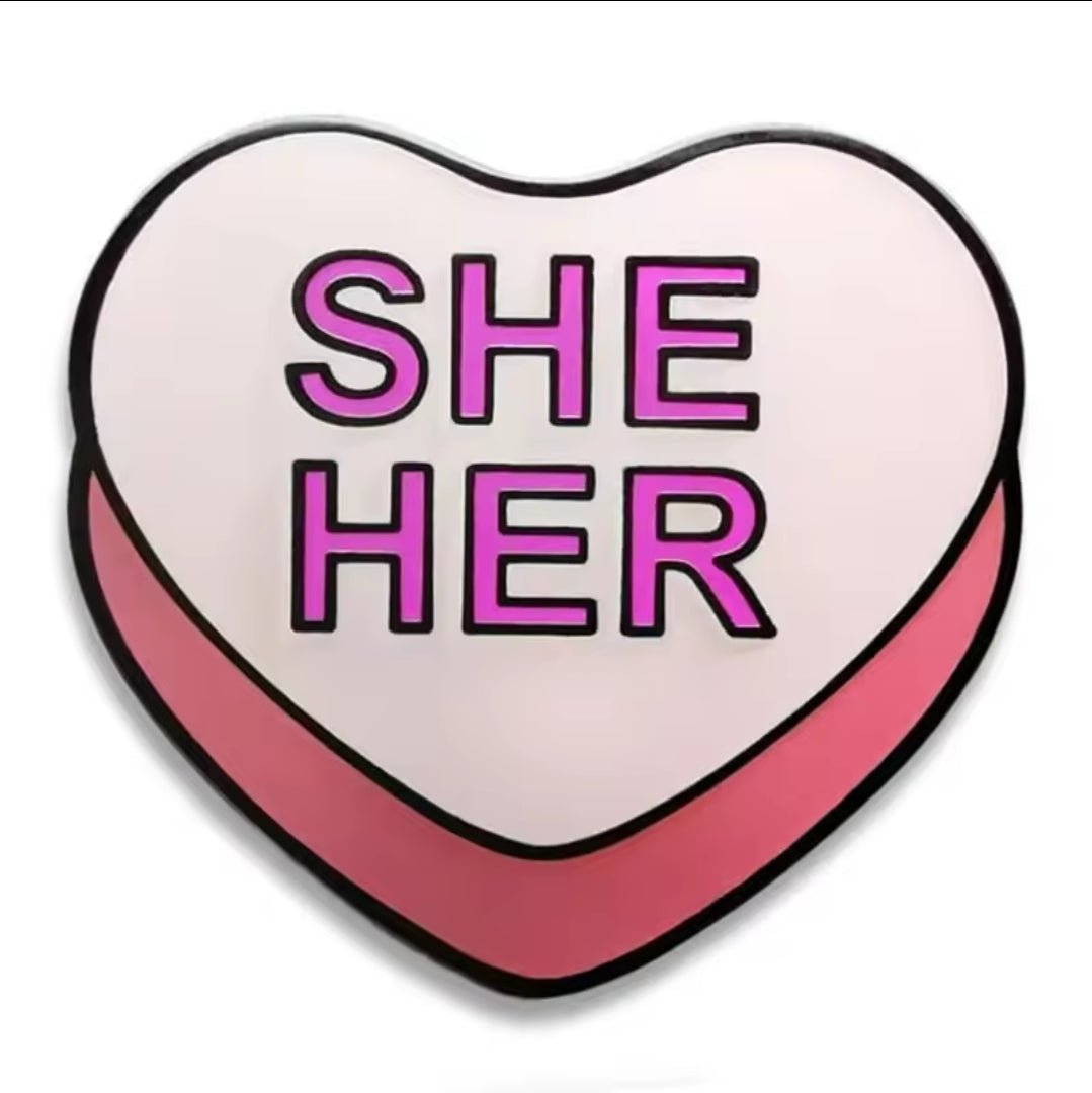 Show your identity with the Kiss Me Later She/Her Pronoun Pin—a pink heart enamel pin with a bold pink border and SHE HER in uppercase on a light pink background.