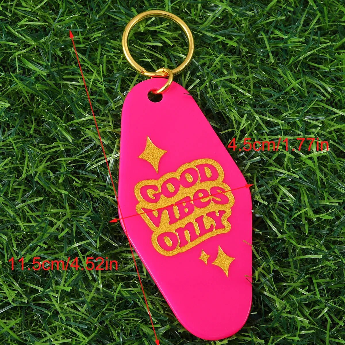 A pink hotel key ring with gold GOOD VIBES ONLY text and stars lies on grass. Red lines show its size: 11.5 cm x 4.5 cm (4.52 in x 1.77 in). Worldwide shipping available!.