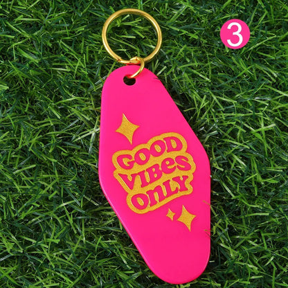 A 12cm bright pink hotel key ring with Good Vibes Only in yellow text and gold stars, shown on green grass. Pink circle with number 3 at top right. Worldwide shipping available.