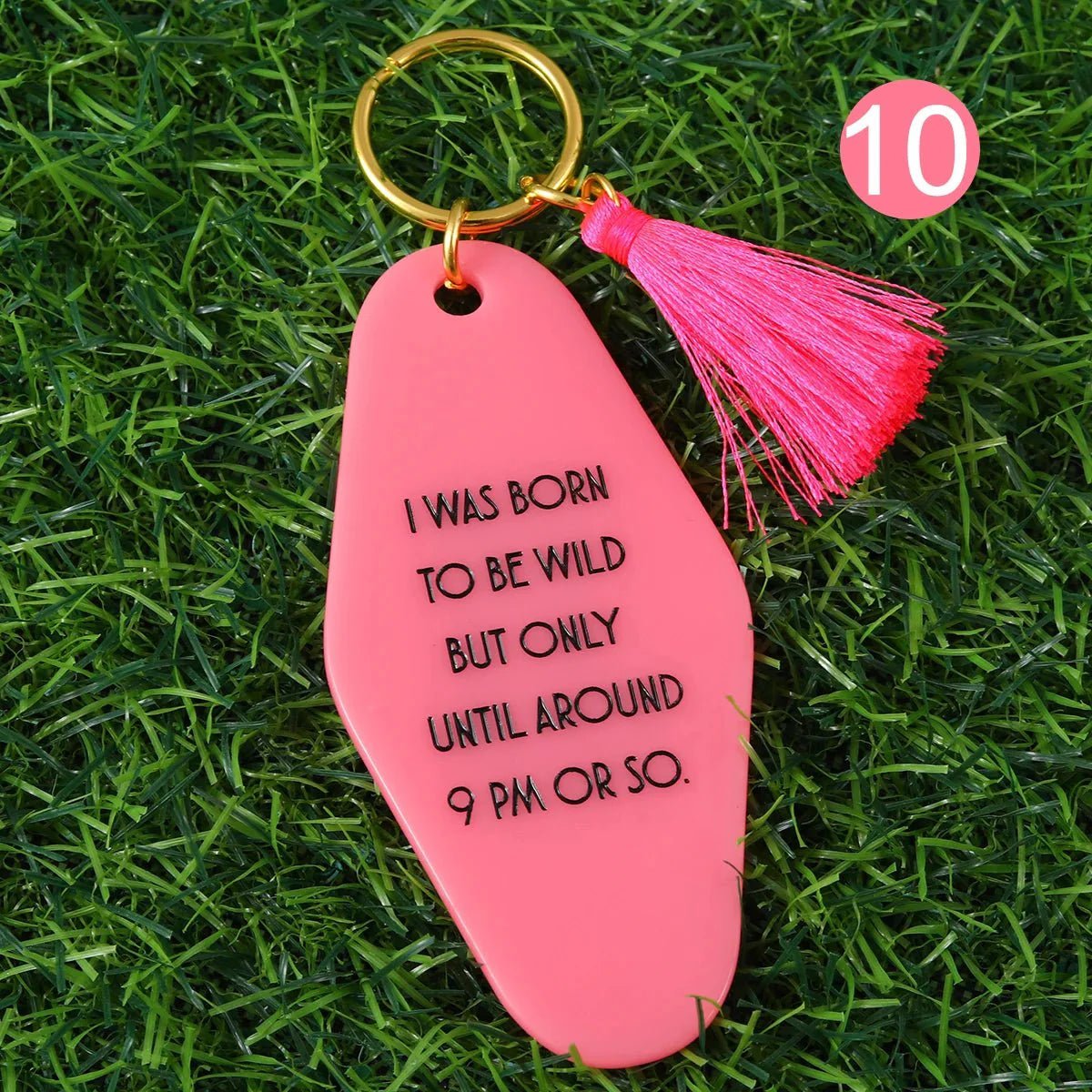 A 12cm pink key ring with a tassel  rests on grass, reading I was born to be wild but only until around 9 PM or so. A pink circle with the number 10 is in the top right. Enjoy worldwide shipping!.