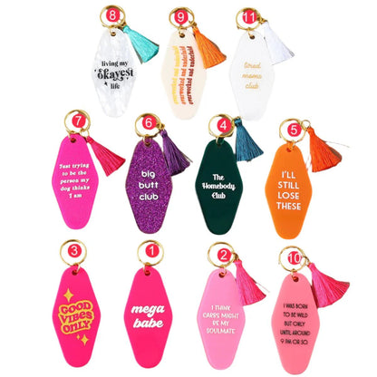 Ten colorful hotel key rings with tassels, each showing a unique funny message in bold pink, orange, purple, white, or yellow. Each 12cm ring is arranged in two rows and available for worldwide shipping.