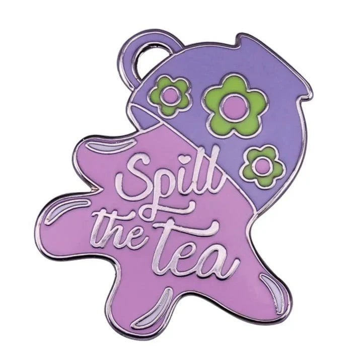 The My Cutesy Era enamel pin features a tilted purple teapot with green flowers, pouring light purple liquid that spells Spill The Tea in cursive. Ideal as a gift and available for worldwide shipping.