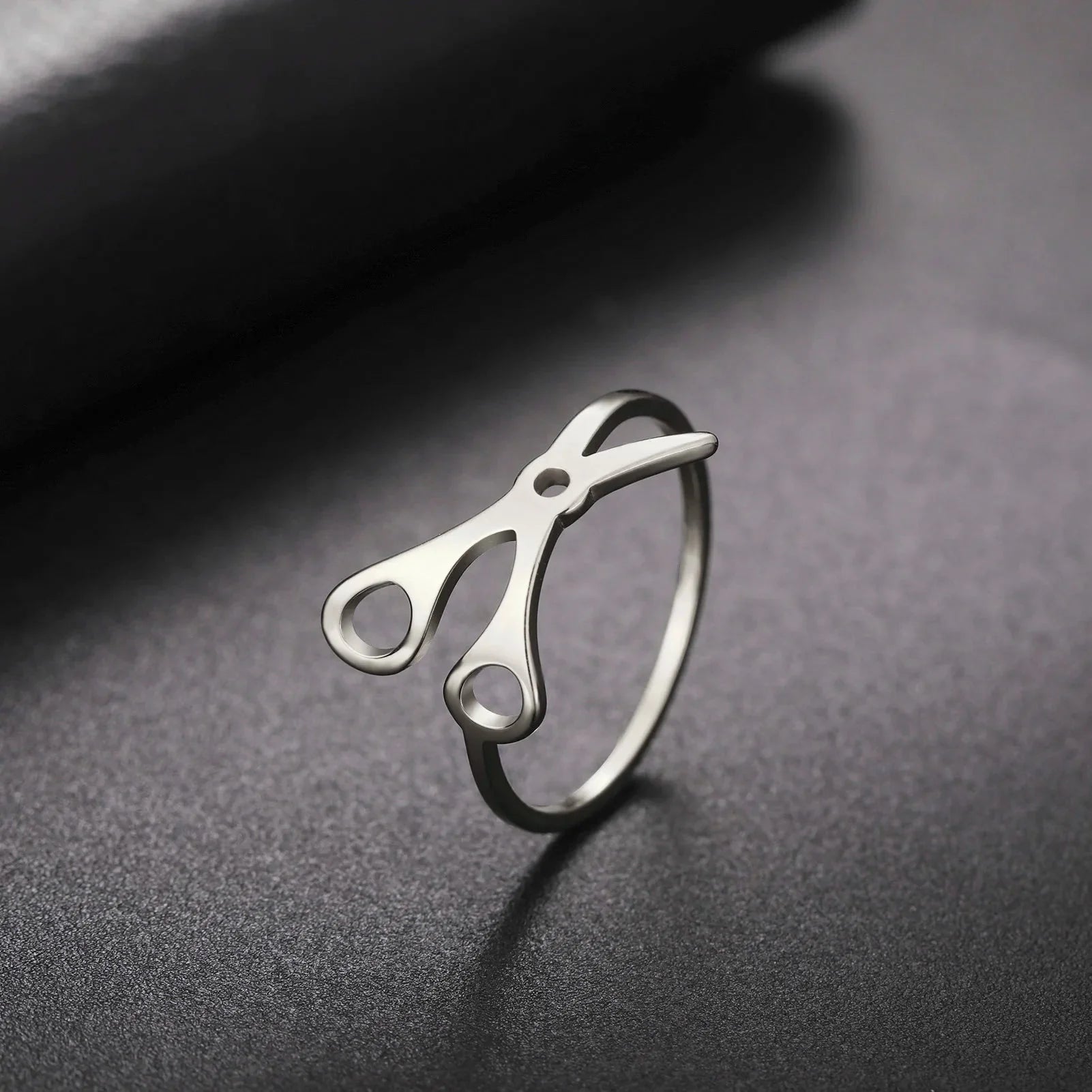 Scissor Ring, crafted in stainless steel, features scissor handles and blades on top—making it a standout sapphic pride accessory on any smooth, dark surface.