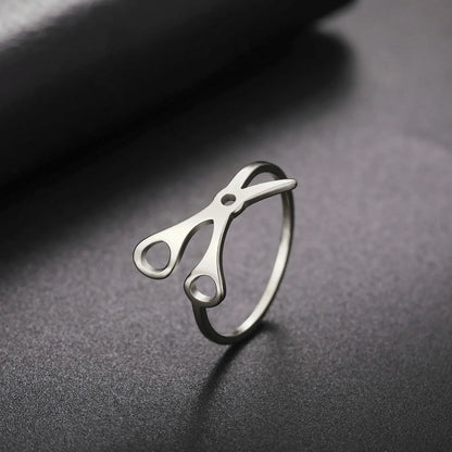 Scissor Ring, crafted in stainless steel, features scissor handles and blades on top—making it a standout sapphic pride accessory on any smooth, dark surface.