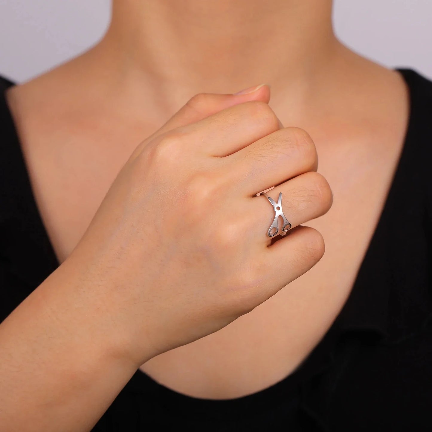 A person wears a silver Scissor Ring, shaped like scissors, on their ring finger near their chin. Its stainless steel design makes it a unique sapphic pride accessory, styled with a sleek black top.
