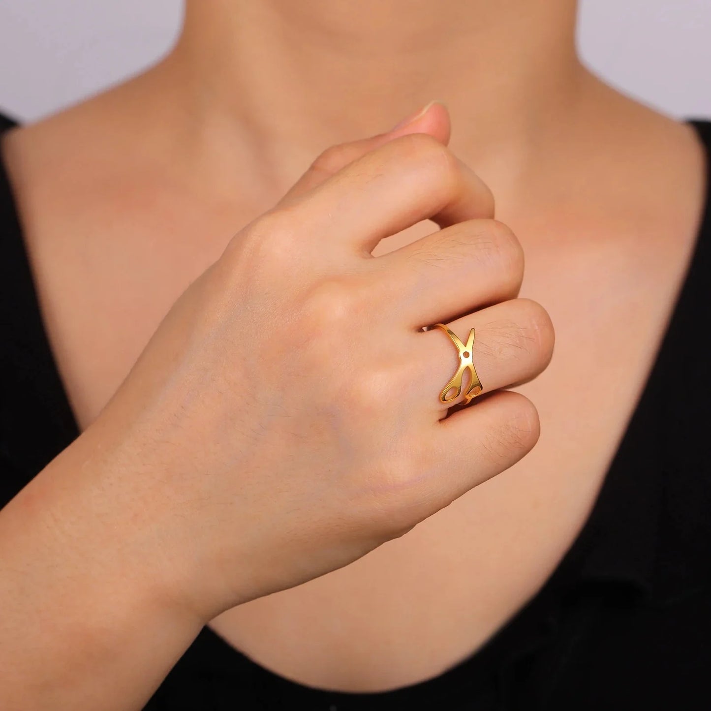 Someone wearing a gold Scissor Ring with an abstract design on their middle finger, hand near chin against a plain background—a striking sapphic pride accessory for those seeking something bold and unique.