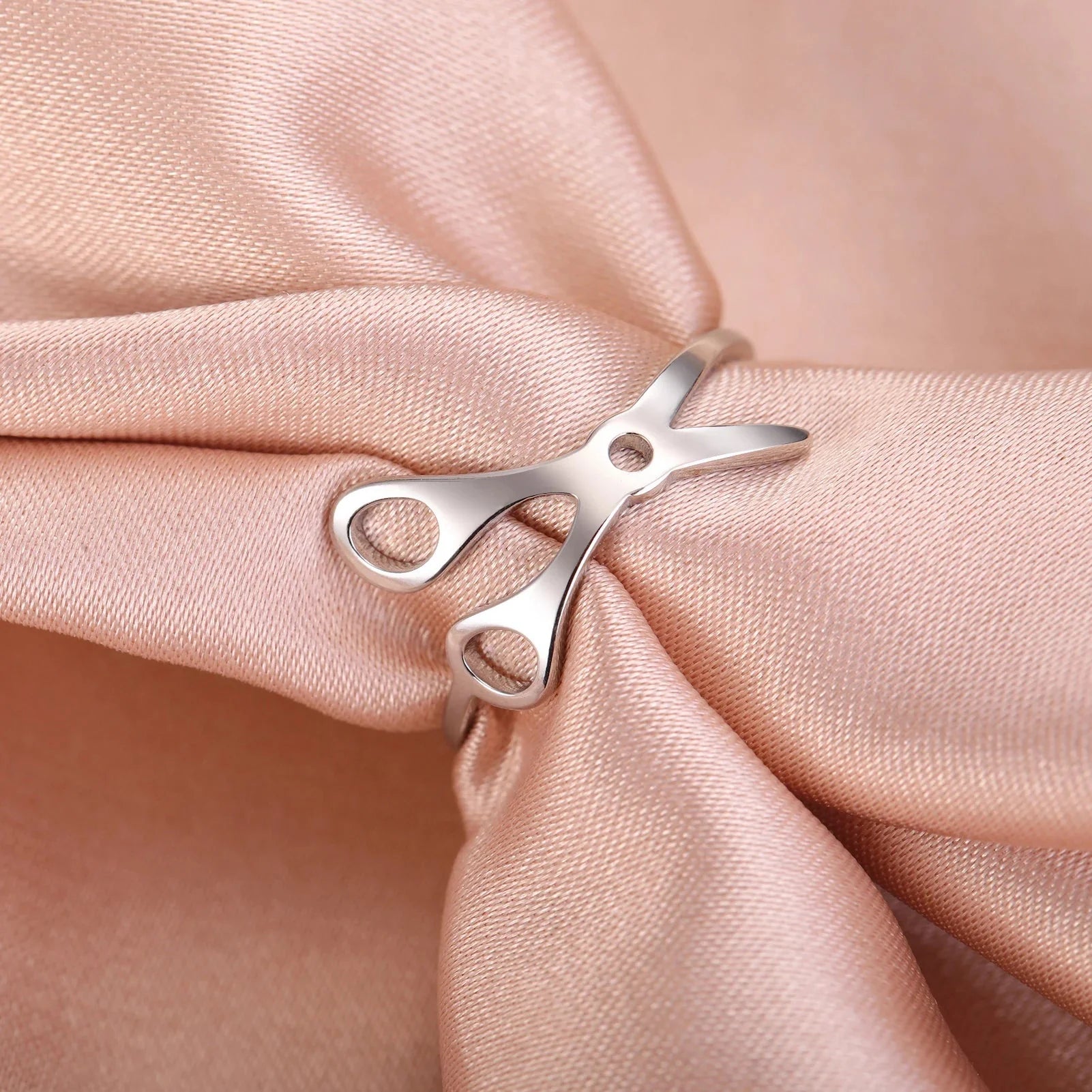 Scissor Ring made from stainless steel rests on soft, pale pink satin fabric.