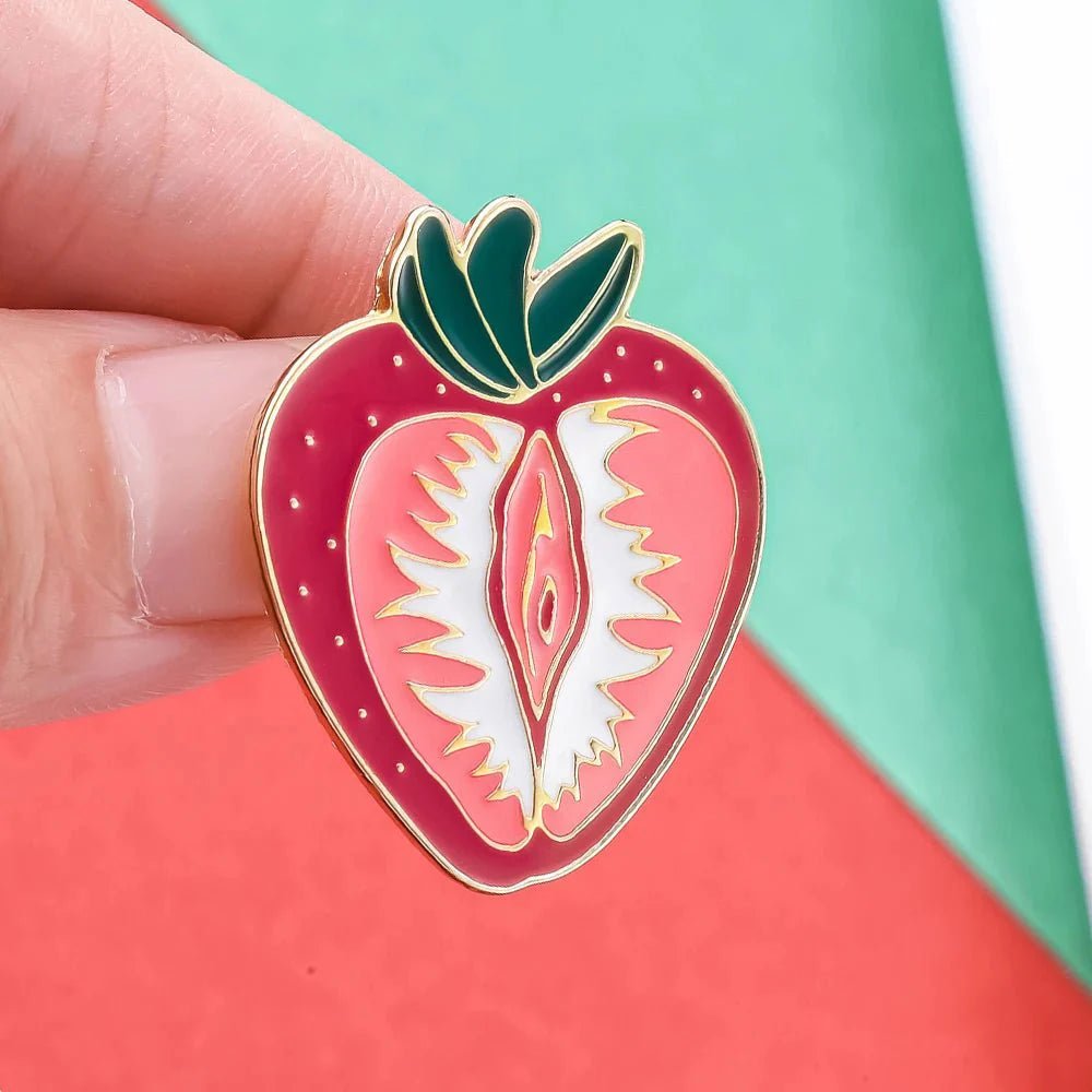 A hand displays the Strawberry Vulva pin, a playful feminist enamel accessory featuring a vulva-shaped strawberry on a green and red background—perfect for sapphic WLW lesbian pride and body positivity.