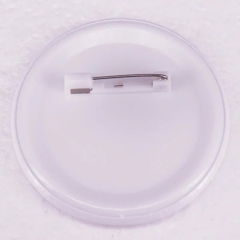A close-up of the back of a round, white Gay Skate button badge with a metal safety pin fastener on a plastic backing, displayed on a textured white surface—ideal for showing your rainbow or trans pride accessory.