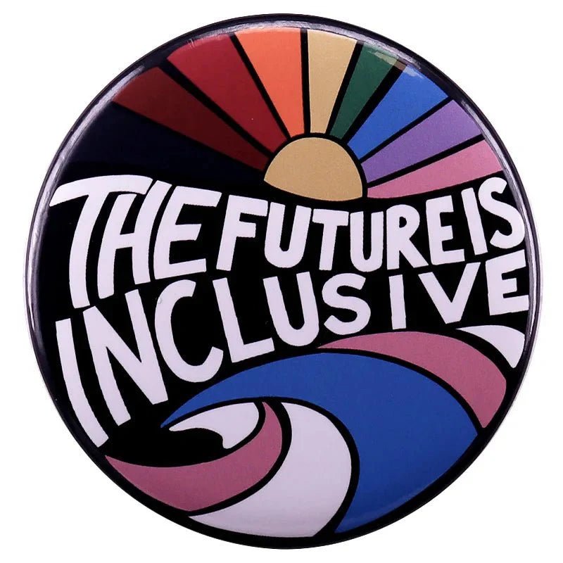 A circular button badge by Kiss Me Later with The Future Is Inclusive in bold, a sunrise in rainbow pride colors on top, and blue, pink, and white stripes below to represent trans pride.