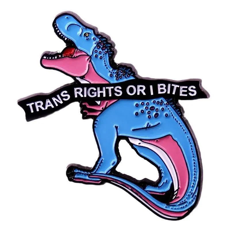 Enamel pin features a blue and pink cartoon dinosaur holding a black banner in its teeth that says TRANS RIGHTS OR I BITES, celebrating trans rights with colors inspired by the trans pride flag.