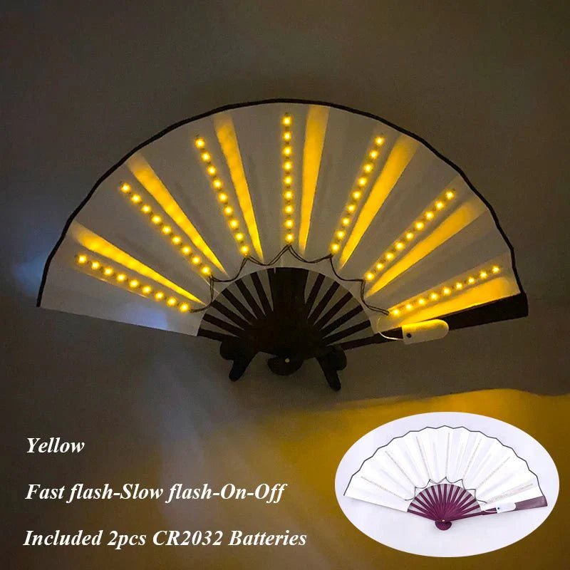 My Cutesy Era white folding fan with yellow LED lights on each rib, shown open and glowing. Features light-up LED, Fast flash/Slow flash/On/Off modes, includes 2 CR2032 batteries. Inset displays the fan unlit.