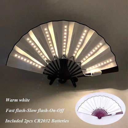 A My Cutesy Era white folding LED fan with built-in warm white lights is shown open. Modes: Fast flash, Slow flash, On, Off. Includes 2 CR2032 batteries. Inset displays the fan closed.