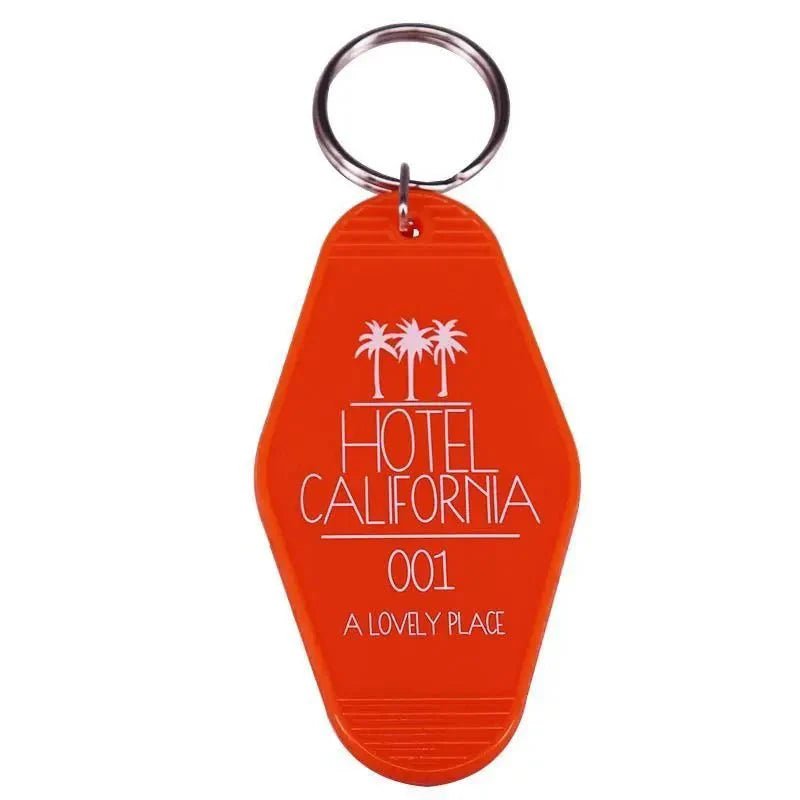 An orange retro hotel key ring by Kiss Me Later features three palm trees and HOTEL CALIFORNIA 001 A LOVELY PLACE in white—a playful pop culture accessory for your keys.