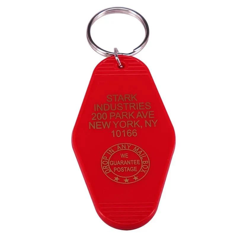 A colourful retro key ring by Kiss Me Later in red with gold text reads STARK INDUSTRIES, 200 PARK AVE, NEW YORK, NY 10166 and features the classic DROP IN ANY MAIL BOX, WE GUARANTEE POSTAGE—a fun pop culture collectible.