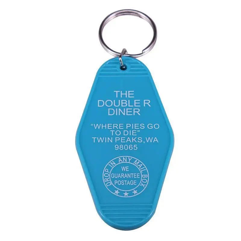 A blue plastic retro hotel key ring by Kiss Me Later, shaped like a motel tag. It reads: THE DOUBLE R DINER, WHERE PIES GO TO DIE, TWIN PEAKS, WA 98065 with a Drop in any mailbox guarantee emblem.