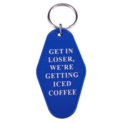 A vibrant blue key ring by Kiss Me Later features white text, GET IN LOSER, WE’RE GETTING ICED COFFEE—perfect for pop culture fans and those who love retro hotel-style accessories.
