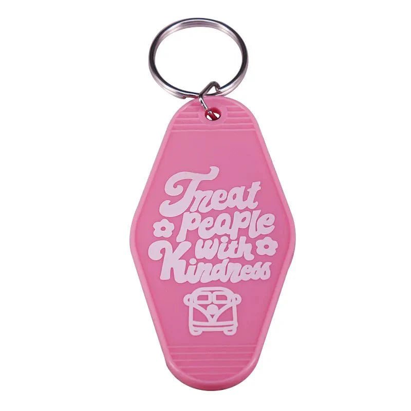 The Kiss Me Later key ring features a vibrant pink design with white Treat people with kindness text and an envelope-heart graphic—ideal for pop culture enthusiasts and fans of retro hotel-style accessories.