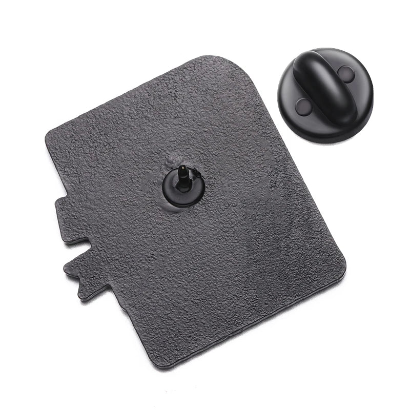 A textured black rectangular patch with a central valve and separate round black plastic cap, both on white—perfect for displaying your favorite enamel pin or showing trans pride. Brand: Kiss Me Later.