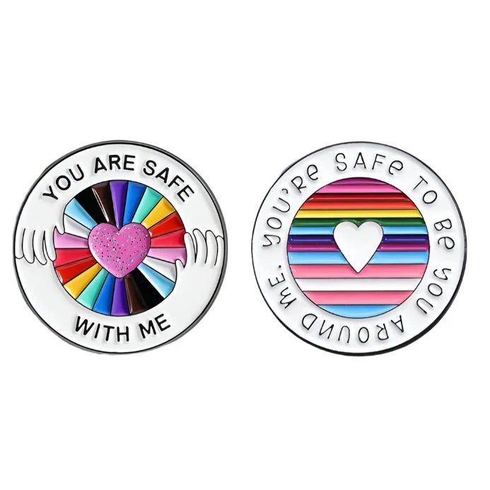 Two circular ainbow pride pins: one with a glittery pink heart, hands, and “You are safe with me,” the other a white heart on rainbow stripes, “You’re safe to be you around me.” LGBTIQ+SB ally pins shipping worldwide.
