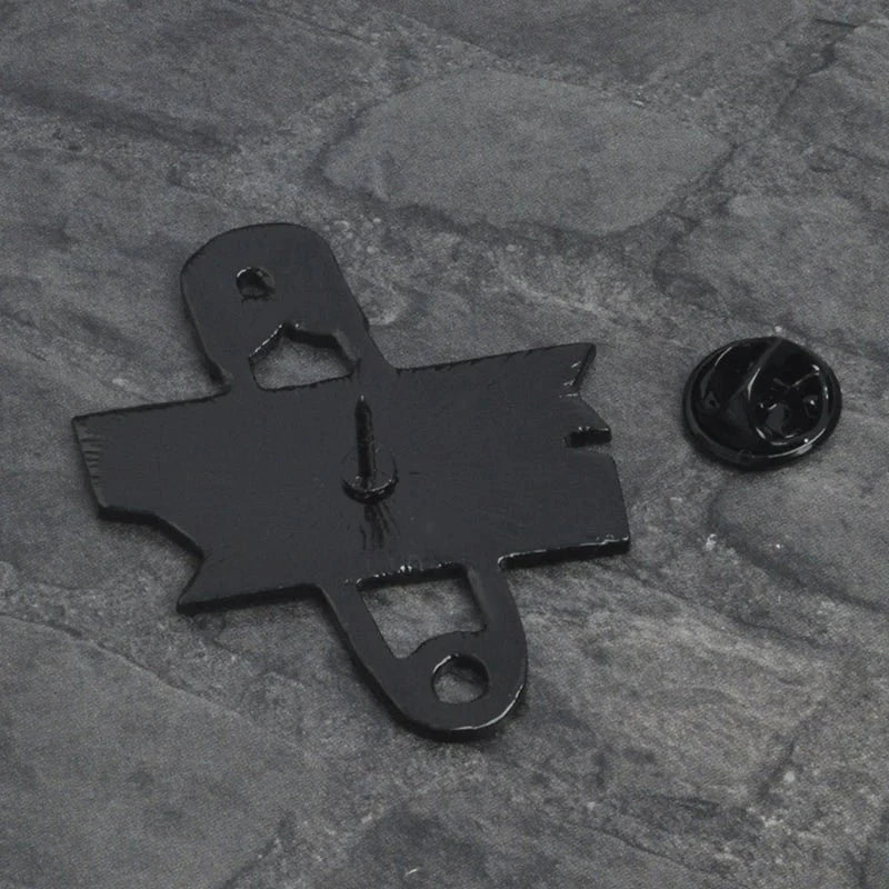 A black metal Bat-Signal pin by Gay Skate is displayed on a gray textured surface with its round backing detached—perfect for pairing with pride accessories or a love heart enamel badge.