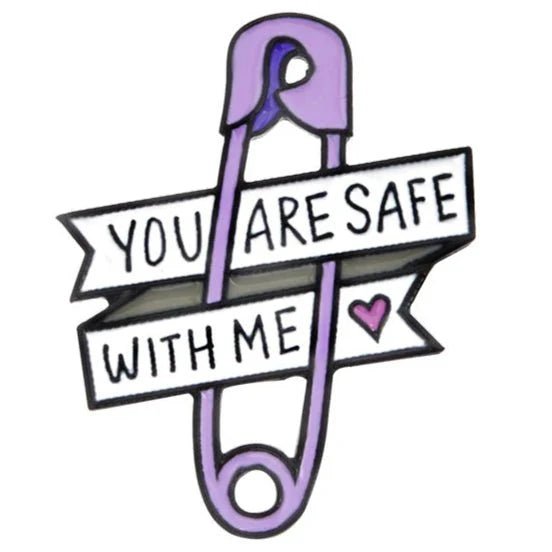 A purple safety pin enamel badge by Kiss Me Later, featuring two white banners with You are safe with me and a small pink heart—perfect for pride events or showing your support.
