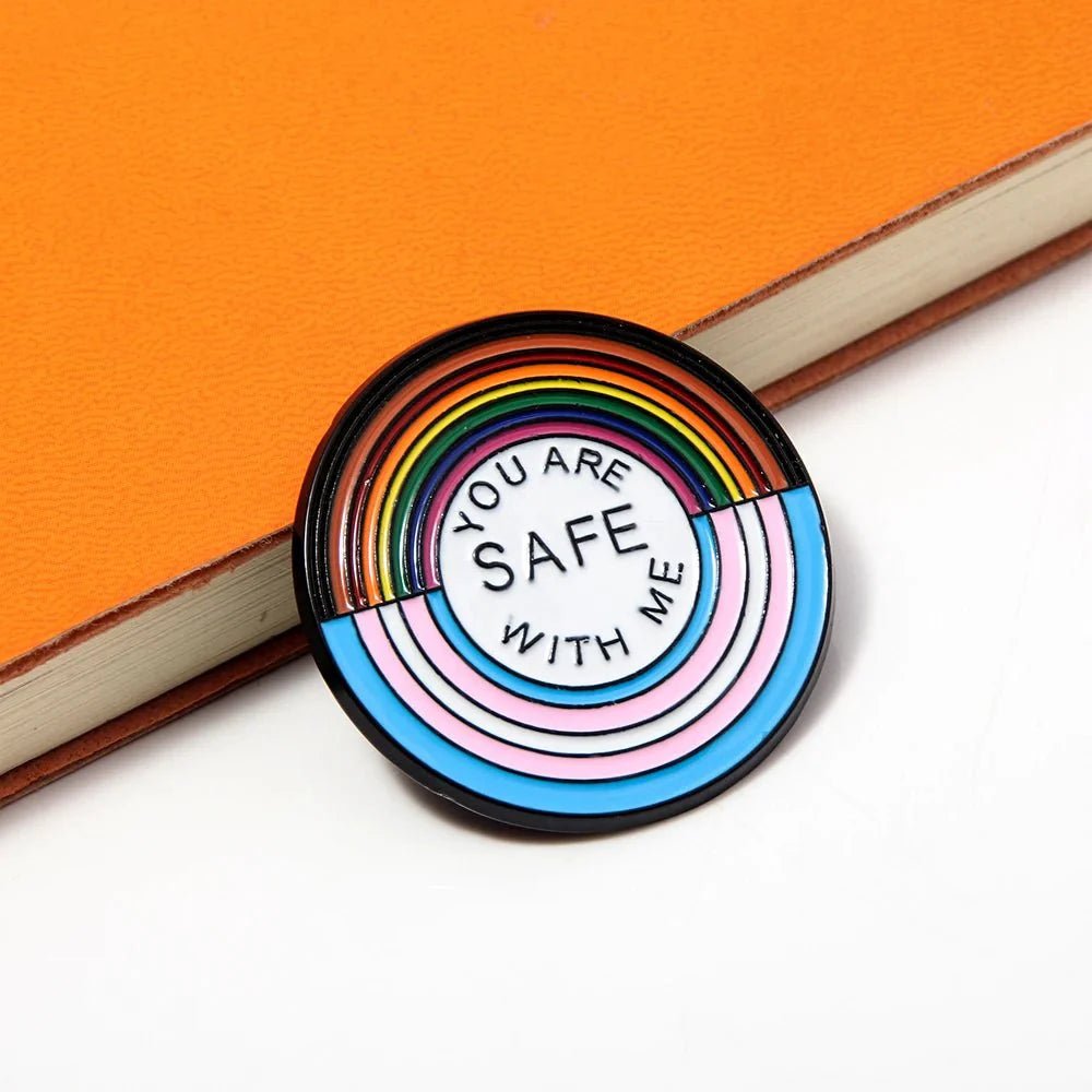 Round rainbow pride enamel badge features pastel stripes and You are safe with me in the center, displayed on an orange notebook. Enjoy worldwide shipping on this thoughtful accessory!.