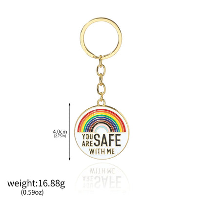Gold keychain features a 4.0 cm round pendant with a rainbow design and YOU ARE SAFE WITH ME text, weighing 16.88g. Inspired by pride enamel badges. Worldwide shipping available.