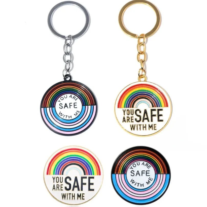 Four rainbow pride enamel badges and keychains with YOU ARE SAFE WITH ME in the center. Each has rainbow stripes; two have silver rings and two have gold. Worldwide shipping available.