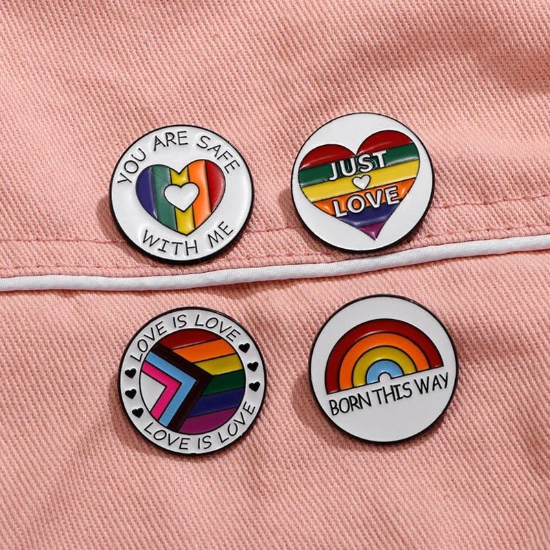 Four round with LGBTQ+ pride symbols and messages like “LOVE IS LOVE” rest on pink fabric. Each rainbow enamel pin celebrates inclusivity, and worldwide shipping lets you share the love anywhere.