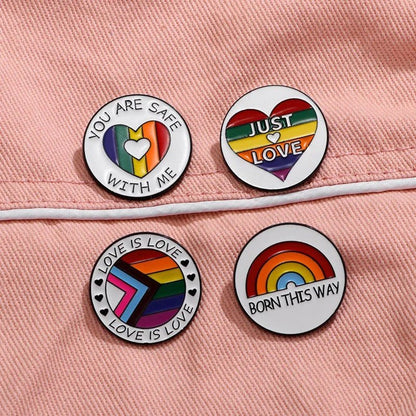 Four round with LGBTQ+ pride symbols and messages like “LOVE IS LOVE” rest on pink fabric. Each rainbow enamel pin celebrates inclusivity, and worldwide shipping lets you share the love anywhere.