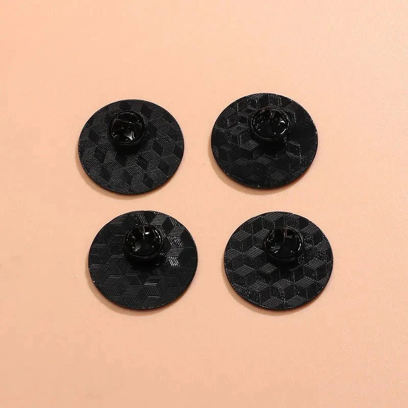 Four round, black textured plastic objects with a central clip are arranged in a square on a light peach-colored surface—ideal for organizing your rainbow pride enamel pin collection, with worldwide shipping available.